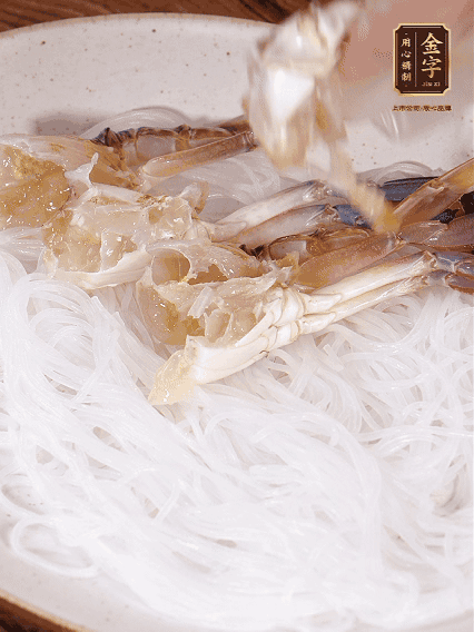 盤底墊上粉絲，擺上梭子蟹、火腿片，撒姜粒，淋上蒸魚豉油、花雕酒調味腌制15分鐘